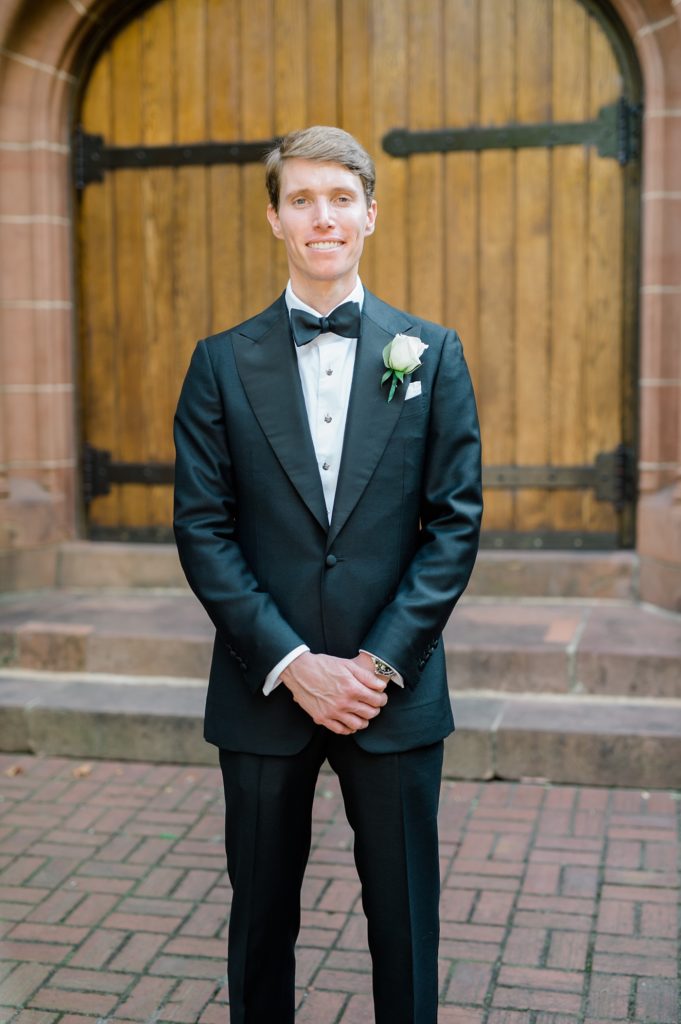 smiling groom standing outside of a church