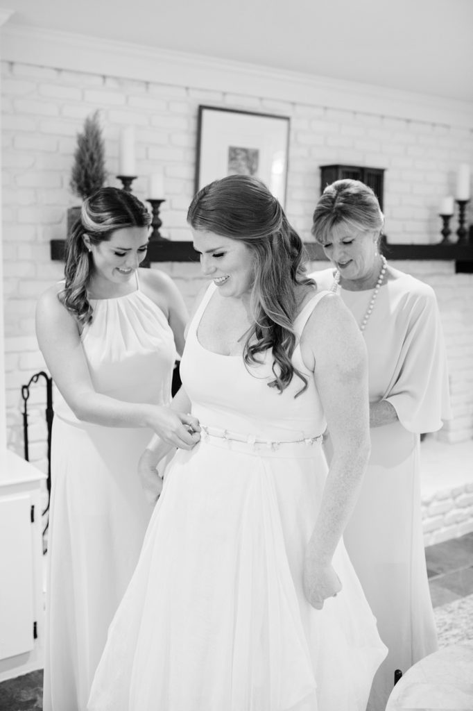 mom and sister helping bride get dressed on her wedding day