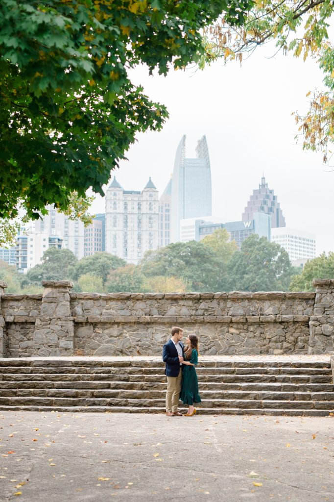 couple infront of the atlanta skyline for their couple smiling and holding their dog for piedmont park engagement photos