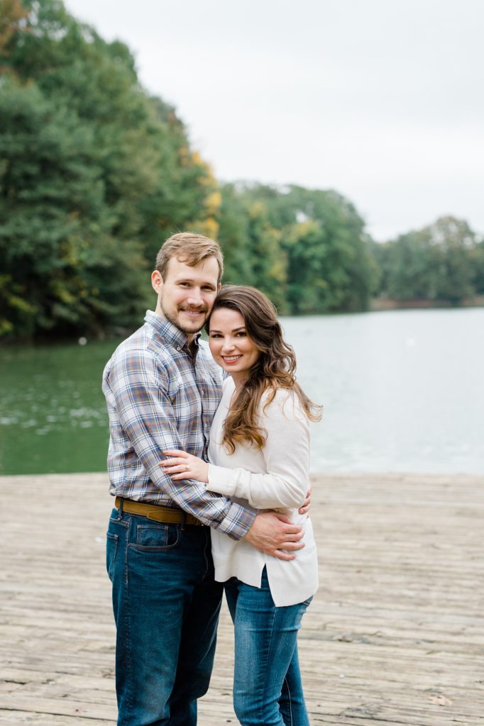 couple hugging for couple smiling and holding their dog for piedmont park engagement photos