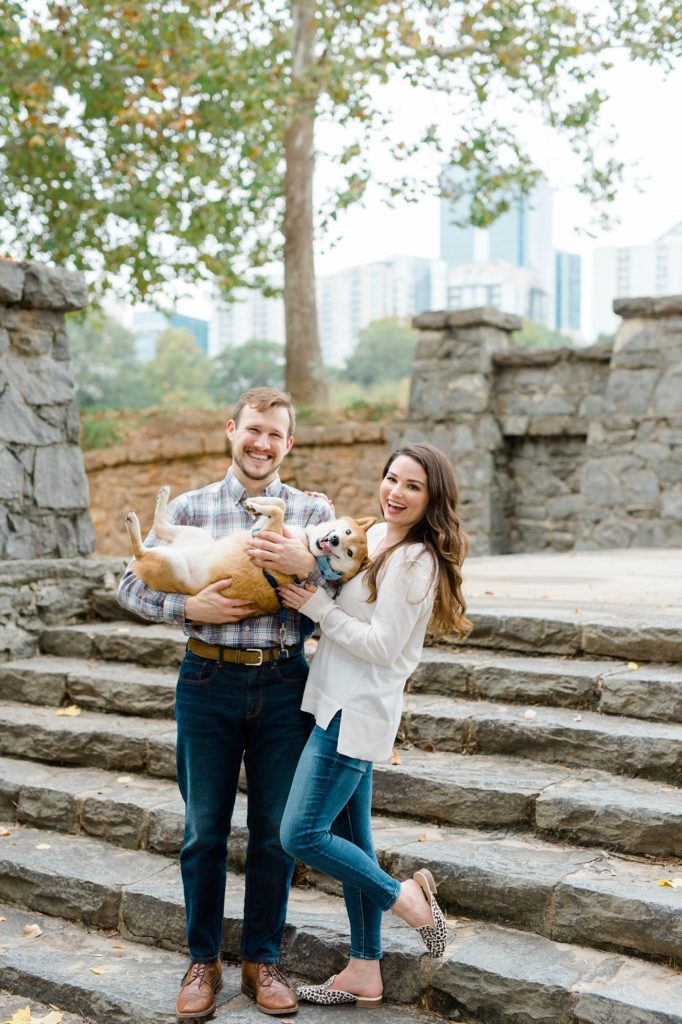 couple smiling and holding their dog for piedmont park engagement photos